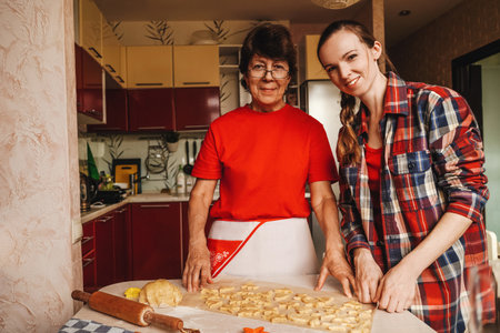 Young woman and senior mother cooking cookies in red clothes.の写真素材