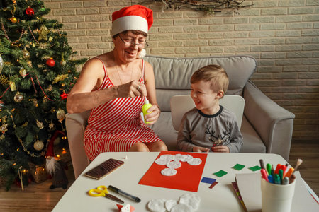 A Little boy with grandmother make Christmas craft, greeting card. Christmas tree and decoration on background.の写真素材