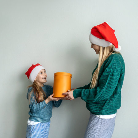 Cute little girl and her beautiful mother in Santa hats hold gift box and surprised. plain backgroundの写真素材