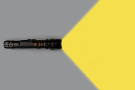 Flashlight turned on with yellow beam light on gray background with empty place for text. Top view. Minimal creative concept. Color 2021.の写真素材