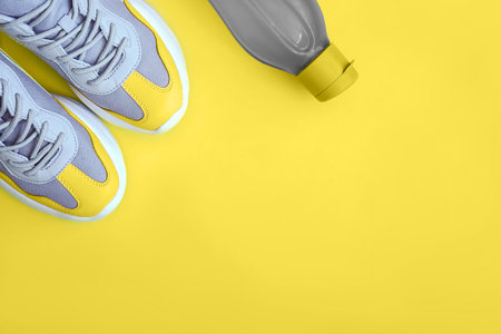 Flat lay yellow sport shoes and bottle of water on yellow background. Concept healthy lifestyle, sport and diet. Copy space.の写真素材