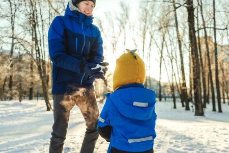 active father and son playing and throw snow in winter park, sunny day.の写真素材