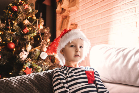 Boy in christmas hat at home near christmas tree in the evening.の写真素材