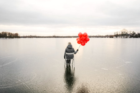 Woman with red balloons outdoor alone. The concept of Valentines day loneliness. Ice river landscape...