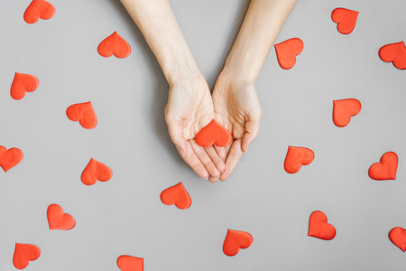 Red hearts pattern on a gray background. Hands hold one red heart.の写真素材