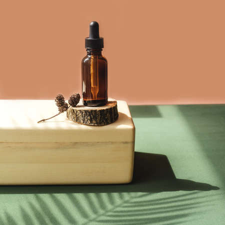 Blank amber glass bottle with face serum on wooden brick. Natural organic cosmetics, herbal essence, sustainable lifestyle concept. Front view, copy space. Decor with palm leaf shadow, saw cut.の写真素材