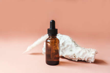 Blank amber glass essential bottle with face serum on beige background. Natural organic cosmetics, sustainable lifestyle concept. Front view, copy space. Decor with stones. Minimalism.の写真素材