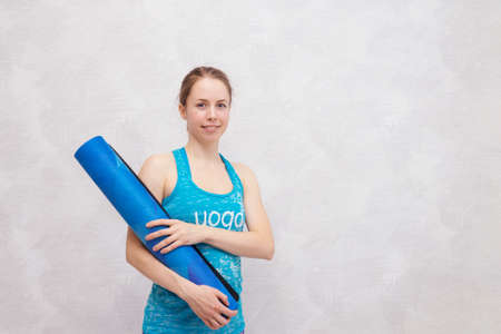 Smiling woman with a blue mat on light backgrond. Look into camera. Place for text.の写真素材