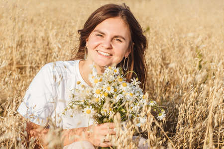 Portrait of the young beautiful smiling woman outdoors in field. Close-up, bouquet chamomile in hands.の写真素材
