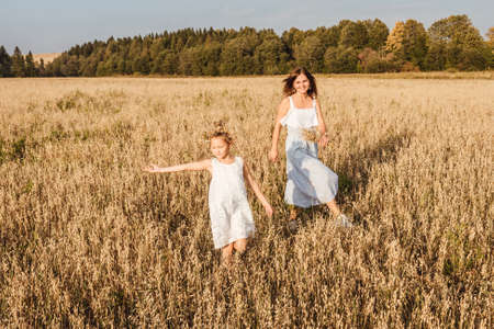 Beautiful young mother and her daughter dance in field. White clothes, freedom concept. Front view.の写真素材
