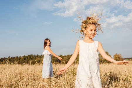 Beautiful young mother and her daughter dance in field. Girl with wreath on the head. White clothes, freedom concept. Front view.の写真素材