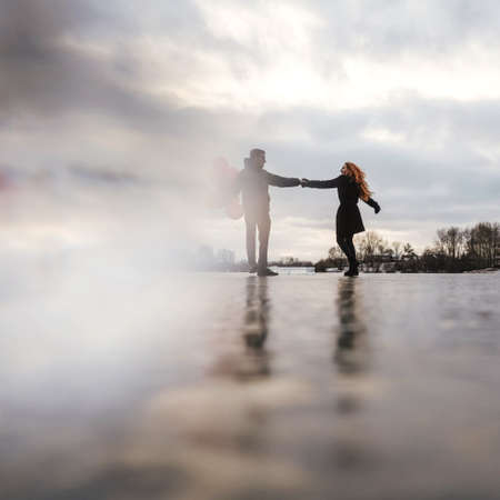 Love couple dance with red balloons outdoor on sky background. Sunset light, black casual clothes. Blurred defocused concept.の写真素材