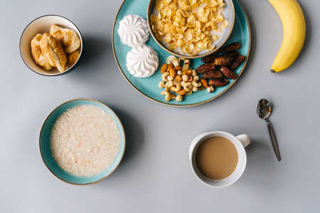 Bright breakfast on gray background, top view. Tasty oatmeal, banana, muesli, nuts, marshmallows and cup of coffee.の写真素材