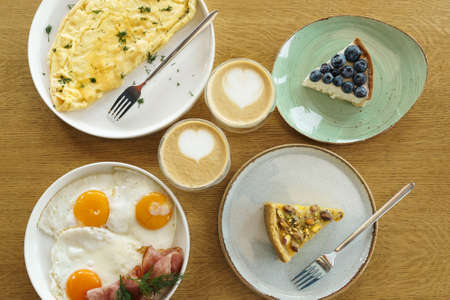 Bright breakfast on brown wooden background, top view. Tasty desserts, omelette and fried eggs and cup of coffee.の写真素材