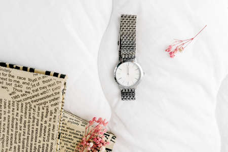 Silver watch on white textile top view. Dry branch of flowers and books as decoration.