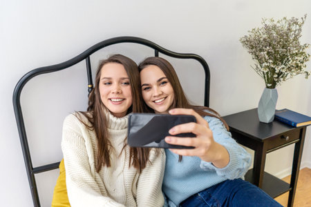 Pretty young women friends taking selfie sitting on bed.の写真素材