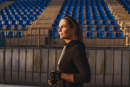 Young woman in black sport suit run at a track stadium. Sun on face.の写真素材