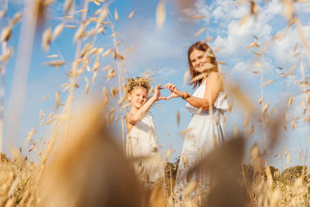 Beautiful young mother and her daughter having fun at the field and make heart from hands. Dry grass on foreground, sky background. White clothes.の写真素材