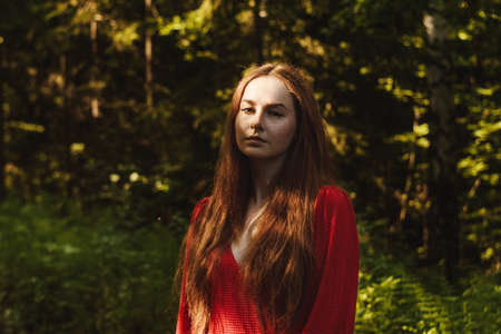 The young woman in red dress in green rainfores. Concept of nature and happy life, adventure. Beautiful light only on face. Fairy tale concept.の写真素材