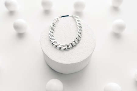 Imitation jewelry, silver bijouterie chain bracelet on white background. White podium and little spheres around.の写真素材