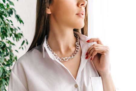 Silver bijouterie chain on woman neck. White background with green plant.の写真素材