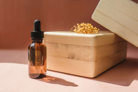 Blank amber glass bottle with face serum near wooden brick. Front view, copy space.の写真素材