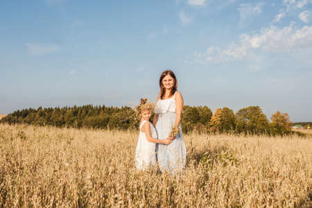 Young mother and daughter stand in field.の写真素材