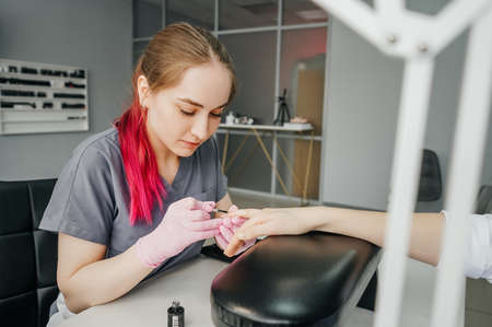 Process of manicure in salon. Professional manicurist woman with pink hair provides service to the client.の写真素材