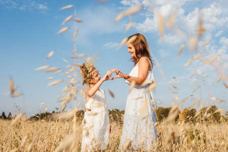 Beautiful young mother and her daughter having fun at the field and make heart from hands.の写真素材