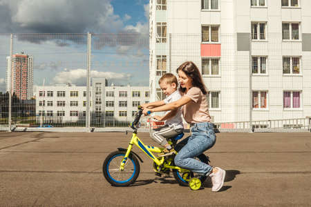 boy rides a bike with his mother. Houses on background, summer.の写真素材