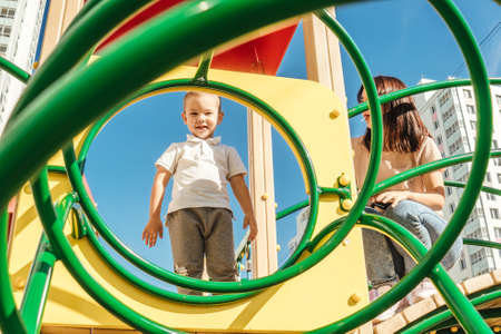 Young happy toddler boy stand on walk, summer. Bottom view, shot through the green playground.の写真素材