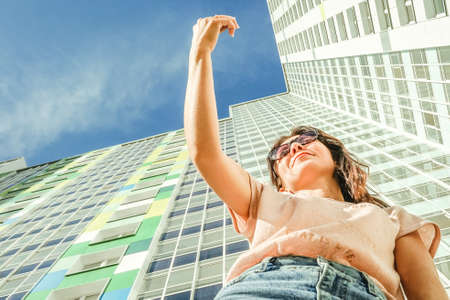 Summer portrait woman with mobile phone, bottom view. Modern house and blue sky on background.の写真素材