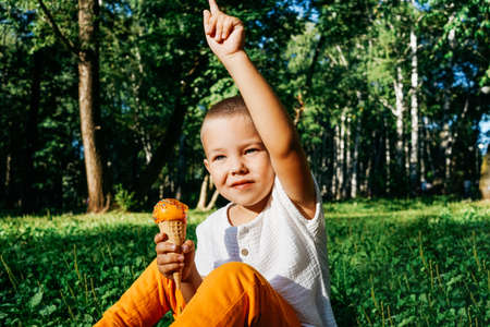Happy kid boy eating orange ice cream.
