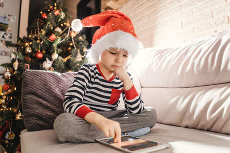 Boy play on tablet near christmas treeの写真素材