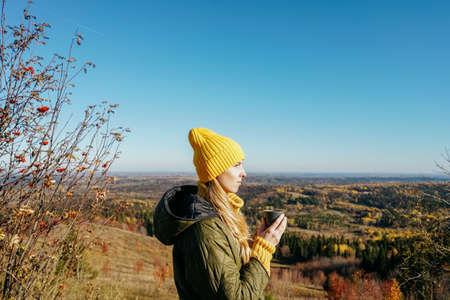 Young woman in yellow green clothes standing in mountain and drink hot tea.の写真素材