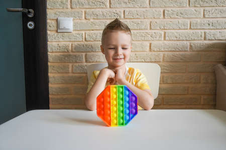 Boy looking at silicone colorful antistress pop toy on the table.の写真素材