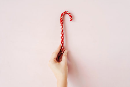 Christmas candy cane in hand on pink background.の写真素材