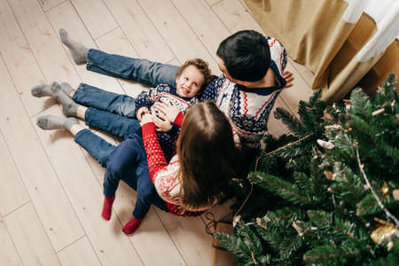 Mom, dad tickle son near christmas treeの写真素材
