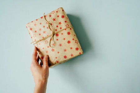 Christmas gift box in hand with red berry branch on blue background. Top view, copy space.の写真素材