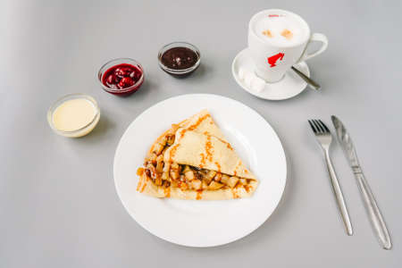 Person eating crepe with apple filling. Tasty breakfast on gray. Different sauces and cappuccino.の写真素材