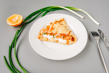 Person eating crepes with filling red fish and cheese. Tasty breakfast on gray background.の写真素材