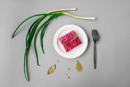 Russian herring salad under a fur coat on gray background. Green onion around plate, top view.の写真素材