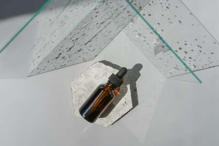 Top view of face serum amber bottle on white background on concrete podium and glass with shadow.の写真素材