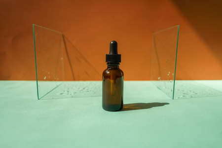 Front view of face serum amber bottle on dual background, pieces of glass with water drops as frame.の写真素材