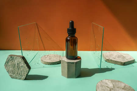 Front view of face serum amber bottle on dual background with concrete podiums and glass.の写真素材