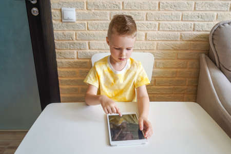 Little boy is playing with digital tablet at home. Boy is sitting at the table and enter password.の写真素材