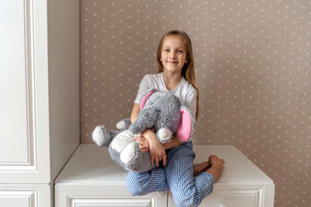 Little girl hugs a stuffed toy at home. Beige wall with white dots, cozy home.の写真素材