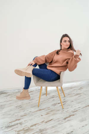 Young attractive woman wearing sweatshirt and jeans on white background studio shot. Woman poses on chair.の写真素材