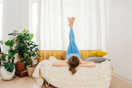 Young woman relax in swing indoor. She lies on her back, legs up.の写真素材