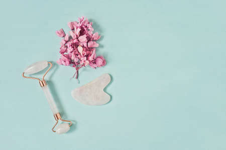 Gua Sha massager and roller from rose quartz on blue background. For face and body care. Flat lay, top view. Copy space.の写真素材